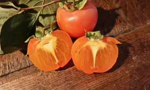 Trois kakis, dont deux coupés en deux, révèlent leur chair orangée. Une astuce pour savoir comment faire mûrir des kakis.