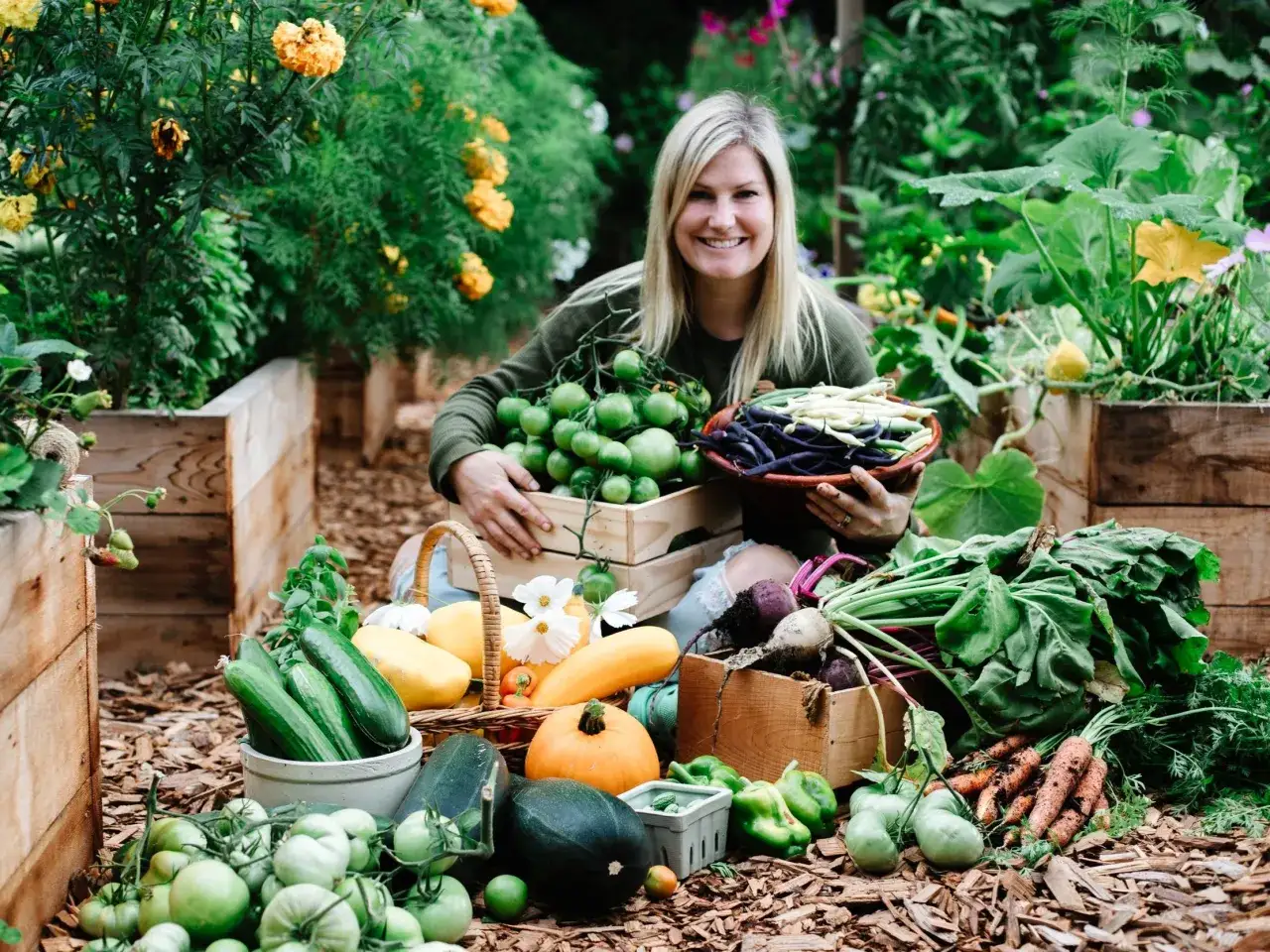 Jolie femme souriante avec une récolte abondante de sa plantation de tomates, haricots, courges et autres légumes frais.